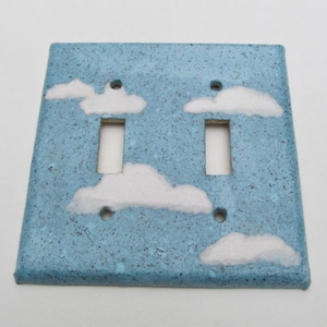 Peut inclure: Une plaque de prise de courant en céramique bleu clair avec un double interrupteur et des nuages peints en blanc.