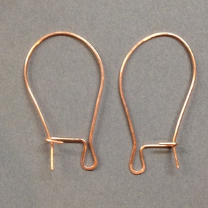 Può includere: Due ganci per orecchini color rame. Ogni gancio ha la forma di una goccia con un fondo ad anello e un perno dritto per l'inserimento. I ganci sono realizzati in filo sottile e liscio e sono esposti su sfondo grigio. Materiali per la creazione di gioielli.