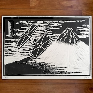 Puede incluir: Una impresión en madera en blanco y negro de un caza X-wing de Star Wars volando sobre una montaña. La impresión está titulada "Star Wars" y está firmada "Junio '22".