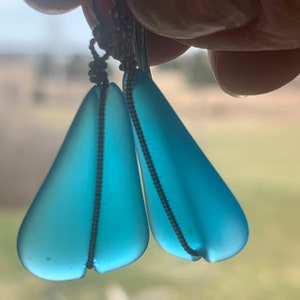 May include: A pair of teardrop-shaped earrings with a frosted blue finish and silver wire accents.