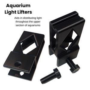 Peut inclure: Deux supports noirs pour éclairage d'aquarium avec un boulon, conçus pour répartir la lumière dans les aquariums. Le texte "Aquarium Light Lifters" est en haut, avec le texte "Aids in distributing light throughout the upper section of aquariums" en dessous.