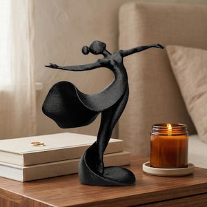 May include: A black sculpture of a dancing figure with arms outstretched and a flowing skirt. The figure has a textured surface and is captured in a dynamic pose with one leg extended, creating a sense of movement and grace in this decorative piece.