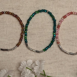 Puede incluir: Tres pulseras de cuentas con cierres plateados. Las pulseras son marrones, verde azulado y rosas.