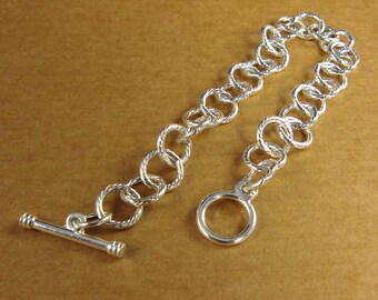May include: A silver chain bracelet with a toggle clasp and a round ring at the end.