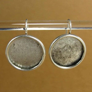 May include: A pair of silver earrings with round, textured, gray metal discs. The earrings are hanging from silver hooks.