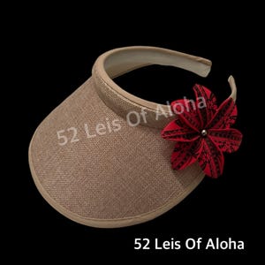 May include: A beige visor with a red and black flower accent. The visor has a white trim and the flower has a silver center. The text "52 Leis Of Aloha" is visible on the visor.