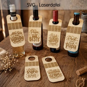 Könnte beinhalten: Wein-Flaschenanhänger aus Holz mit gelaserten Designs und deutschem Text. Die Anhänger sind an verschiedenen Wein- und Bierflaschen befestigt. Die Anhänger tragen Sätze wie "Alles Gute zum Vatertag" und "Papa, du bist der BESTE".