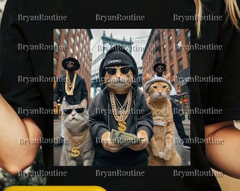 May include: Black t-shirt featuring a graphic of four cats dressed in hip-hop attire, including gold chains and sunglasses. The image includes the text "Canpary" on a hat and "TIANG" on a necklace. The background shows a city scene.