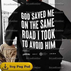 May include: Black oversized t-shirt with white text: "GOD SAVED ME ON THE SAME ROAD I TOOK TO AVOID HIM." Additional text and logos are at the bottom. The shirt is a casual, streetwear style.