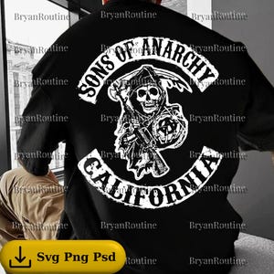 May include: Black t-shirt featuring a white graphic of a grim reaper with a scythe, the words "SONS OF ANARCHY" above, and "CALIFORNIA" below. The design is centered on the back of the shirt.