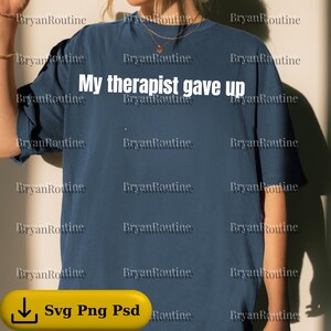 May include: Navy blue t-shirt with the text "My therapist gave up" in white. The shirt has a relaxed fit and short sleeves. The bottom of the image has a yellow bar with the text "Svg Png Psd".