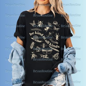 May include: Black t-shirt with cream-colored insect illustrations, including butterflies and beetles. The text "be kind to all kinds" is arranged in a circular design. The shirt is a casual wear item.