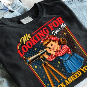 May include: A black t-shirt featuring a graphic of a person with brown hair wearing a red and white checkered shirt and a blue dress, looking through a telescope on a tripod. The text reads: Me LOOKING FOR Who the ASKED YOU.