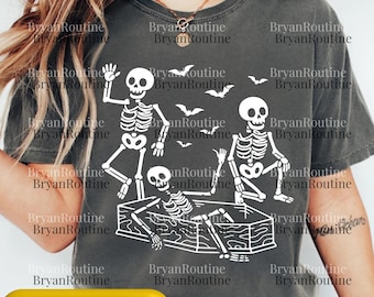 Peut inclure: T-shirt gris foncé avec un motif blanc de squelettes et de chauves-souris, parfait pour Halloween. Le motif comprend trois squelettes dans diverses poses, dont un dans un cercueil. Le texte "Svg Png Psd" est en bas.