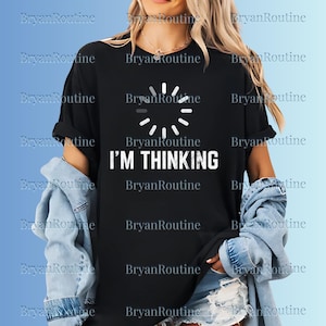 Puede incluir: Camiseta negra con la frase blanca "I'M THINKING" y un icono de carga. Diseño sencillo y humorístico, ideal para un look informal.