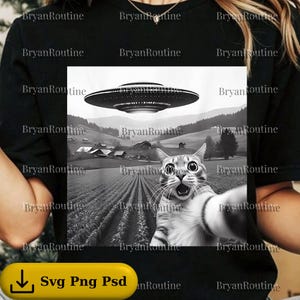 May include: Black and white graphic tee featuring a cat taking a selfie with a UFO in the background. The cat has wide eyes and an open mouth, with a rural landscape behind it. The text "Svg Png Psd" is at the bottom.