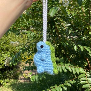 May include: A blue and green crocheted dinosaur hanging ornament with a white string.