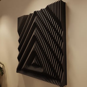 May include: A black, geometric wall art piece with a layered, three-dimensional design. The artwork features a series of angled, parallel lines creating a dynamic, abstract pattern. The piece is mounted on a neutral-colored wall, adding a modern touch to the space.