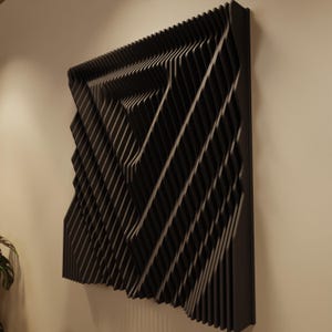 May include: A black, geometric wall art piece with a layered, three-dimensional design. The artwork features a series of angled, parallel lines creating a textured surface. The piece is mounted on a neutral-colored wall, showcasing its modern aesthetic.