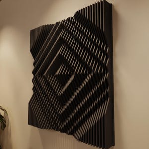 May include: Black geometric wall art with a layered, three-dimensional design. The artwork features a repeating pattern of angled lines, creating a dynamic visual effect. The piece is mounted on a neutral-colored wall, showcasing its modern aesthetic.