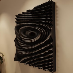 May include: Black, three-dimensional wall art with a layered, wave-like design. The artwork features concentric circular patterns that create a sense of depth and movement. The piece is mounted on a black frame and hangs on a neutral-colored wall.