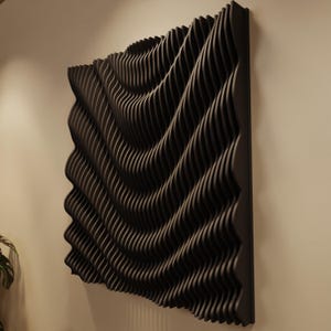 Puede incluir: Una obra de arte mural negra tridimensional con un diseño en forma de ola. La obra está hecha de tiras de madera curvadas y superpuestas, creando una superficie texturizada. La pieza está montada en una pared, mostrando una estética moderna y abstracta.