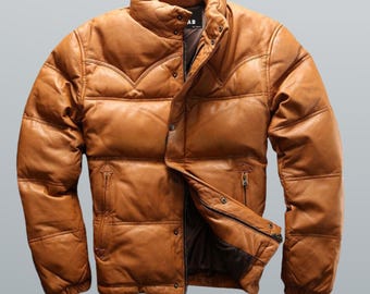 May include: A brown leather puffer jacket with a high collar and a quilted design. The jacket has a button-up front, two zippered pockets, and a soft, padded appearance. The jacket is a warm, stylish outerwear option.