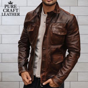 Può includere: Giacca di pelle marrone con collo e quattro tasche frontali. La giacca ha una chiusura con bottoni e viene indossata sopra un maglione grigio chiaro. Il testo "PURE CRAFT LEATHER" è visibile nell'angolo in alto a sinistra.