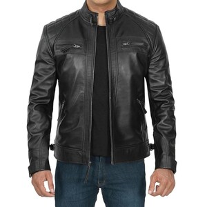 May include: A black leather jacket with a stand-up collar and quilted shoulder detailing. The jacket features two zippered chest pockets, two side pockets, and a front zipper closure. The model is wearing blue jeans.
