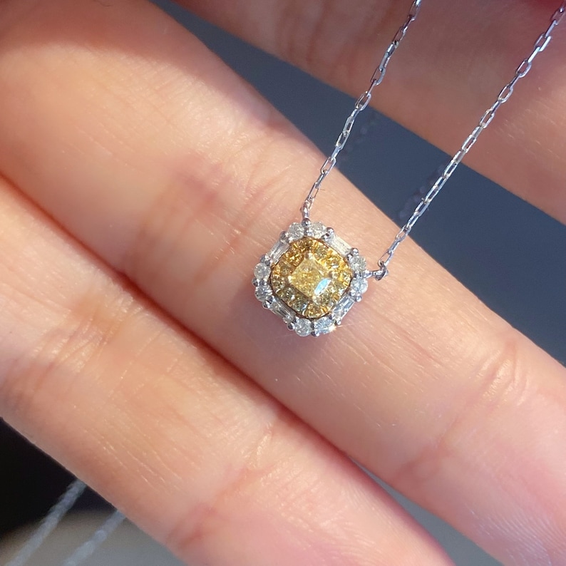 May include: A delicate gold necklace with a square-shaped pendant featuring a yellow diamond surrounded by smaller white diamonds.