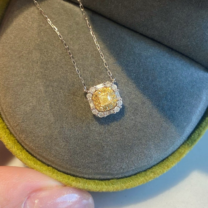 May include: A delicate gold necklace with a square-shaped pendant featuring a yellow diamond surrounded by smaller diamonds.