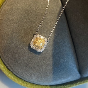 May include: A delicate gold necklace with a square pendant featuring a large, yellow center stone surrounded by smaller diamonds.
