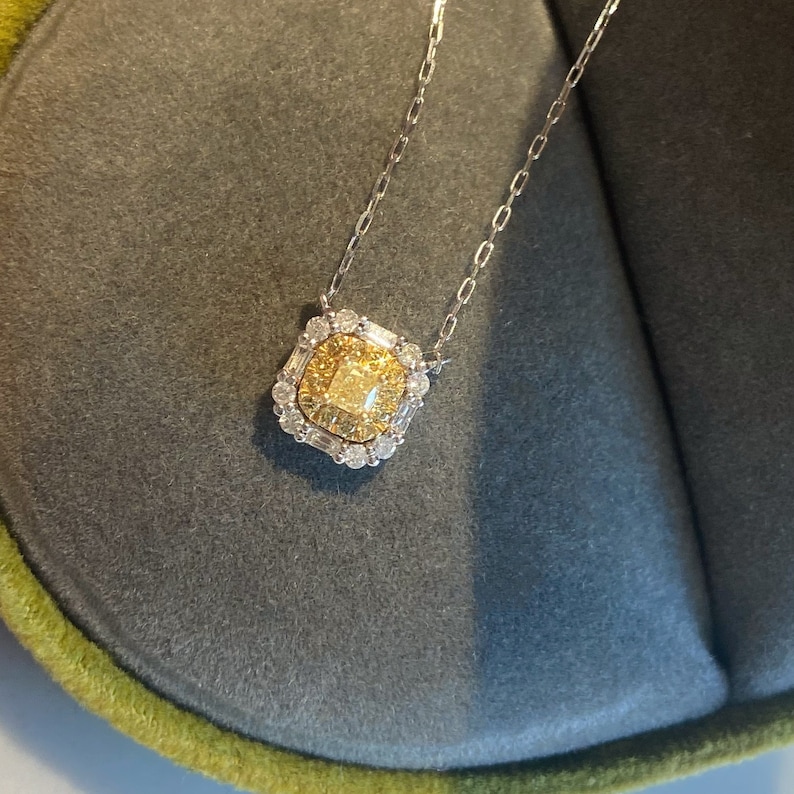 May include: A delicate gold necklace with a square pendant featuring a large, yellow center stone surrounded by smaller diamonds.