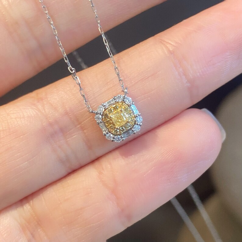 May include: A delicate silver chain necklace with a square pendant featuring a yellow diamond surrounded by smaller diamonds.