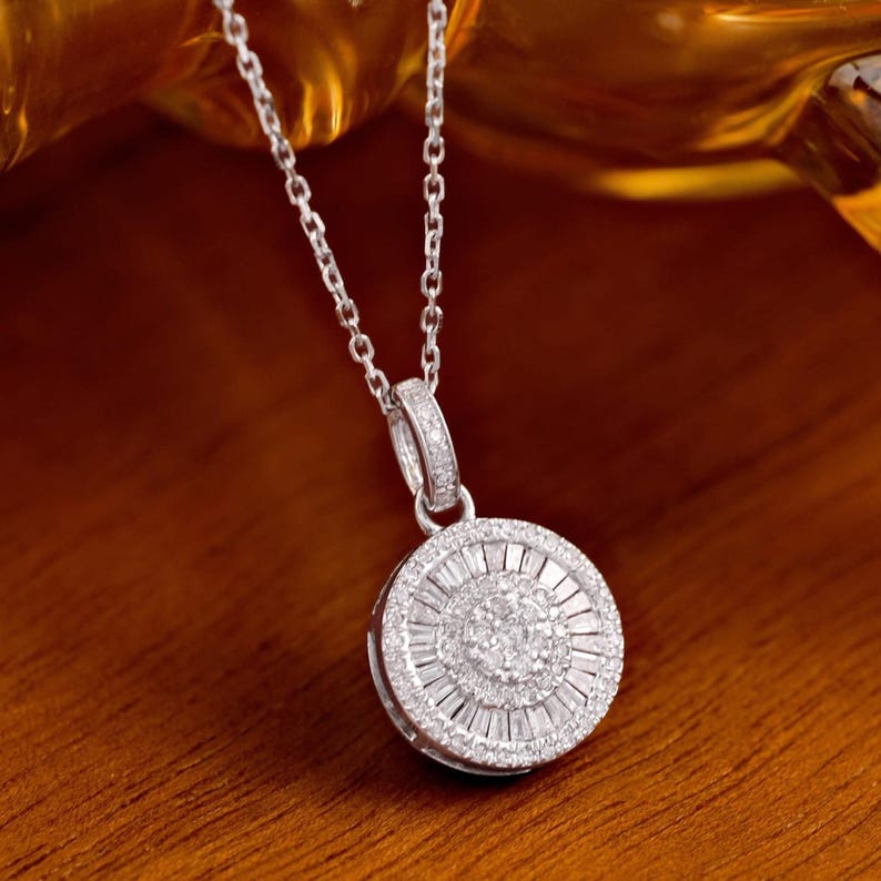 May include: A silver necklace with a round pendant. The pendant is encrusted with multiple small, sparkling stones arranged in concentric circles. The necklace chain is delicate and also silver.