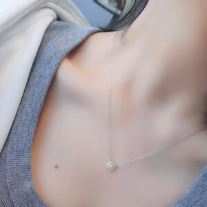May include: A delicate silver chain necklace with a small square pendant featuring a yellow gemstone surrounded by smaller clear gemstones.