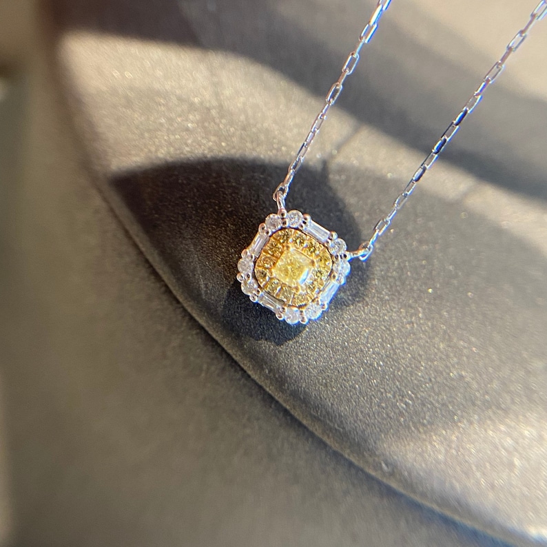 May include: A delicate gold necklace with a square pendant featuring a yellow diamond surrounded by smaller diamonds.