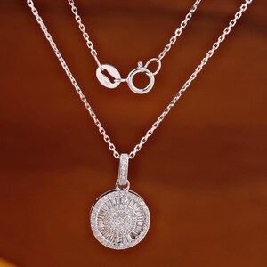 May include: A silver necklace with a round pendant. The pendant is encrusted with small, sparkling stones arranged in a sunburst pattern. The chain is delicate and has a lobster clasp.