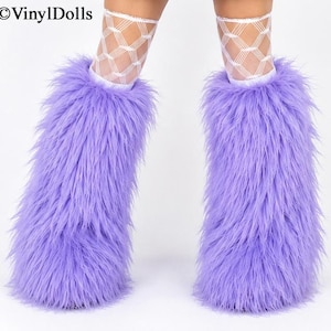 May include: A pair of bright lavender faux fur leg warmers worn over white fishnet stockings. The long-pile synthetic fur covers the lower legs, creating a voluminous, shaggy texture. The text VinylDolls is visible in the upper left corner.