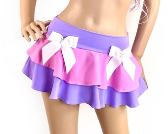 Puede incluir: Una falda de dos niveles en color morado y rosa. La falda tiene un dobladillo con volantes y lazos blancos en cada nivel.