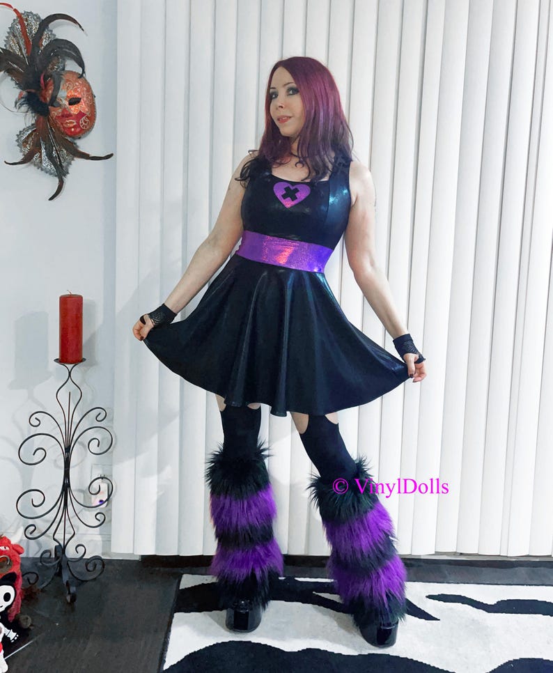 May include: A black mini dress with a purple iridescent belt and a purple heart with a black cross on the front. The model is wearing black tights and purple and black furry leg warmers.