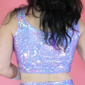 May include: A two-piece iridescent outfit in a light purple color. The top is a cropped tank top and the skirt is a mini skirt. Both pieces are made of a shiny, sparkly fabric.