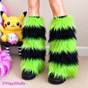 May include: A pair of neon green and black striped faux fur leg warmers worn over black platform shoes. The long-pile synthetic fur features alternating horizontal bands of bright neon green and deep black, creating a bold, textured appearance.