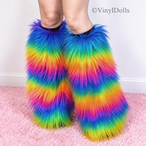 Può includere: Un paio di scaldamuscoli in pelliccia sintetica color arcobaleno con lunghe fibre arruffate a strisce orizzontali blu, verdi, gialle, arancioni e rosa. Il testo VinylDolls è visibile nell'angolo in alto a destra dell'immagine.