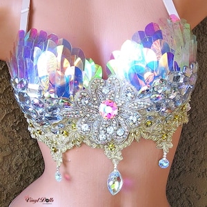May include: A iridescent blue and purple bra with a large flower design in the center. The flower is made of rhinestones and has a pink center. The bra has a gold lace trim and is decorated with iridescent sequins.