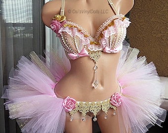 Puede incluir: Conjunto de lencería rosa y dorada con falda tutú. El sujetador está adornado con perlas, encaje y detalles dorados, y presenta un colgante de cristal. El tutú es rosa con purpurina dorada, y el conjunto está adornado con rosas rosas.
