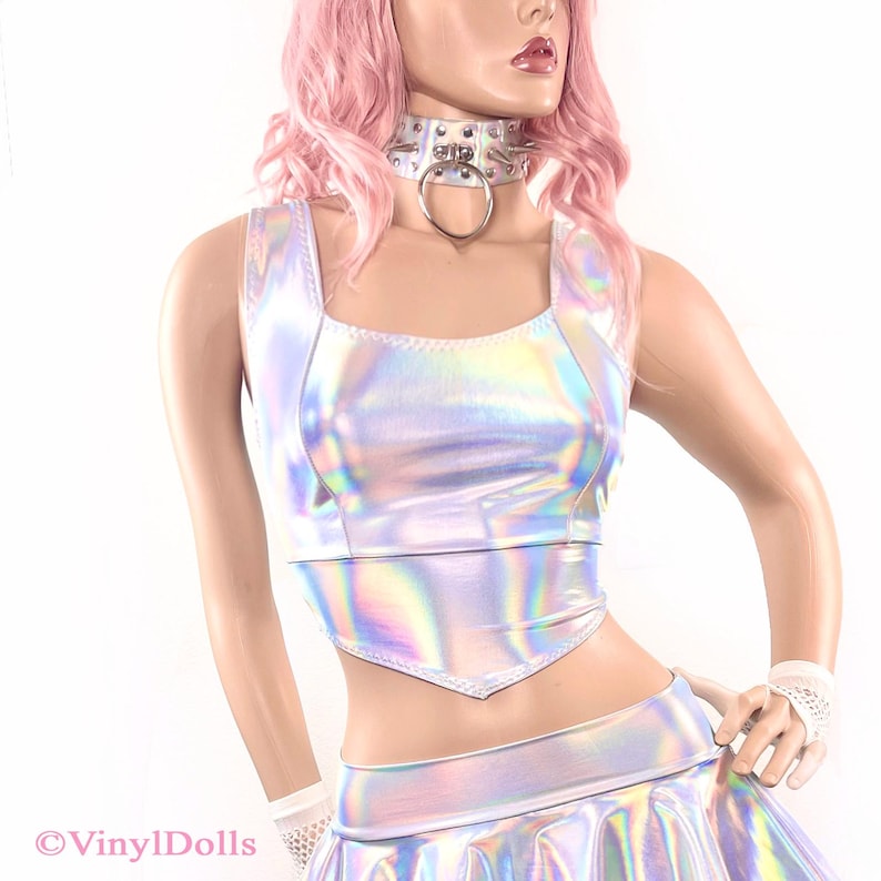 May include: A silver iridescent crop top with a square neckline and a pointed hem. The top is made of a shiny, holographic material.