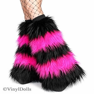 May include: A pair of leg warmers featuring long, shaggy faux fur in alternating horizontal stripes of black and vibrant hot pink. The leg warmers have a solid black elastic band at the top and are displayed on lower legs wearing black fishnet stockings.