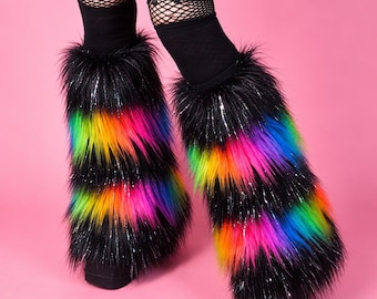 May include: A pair of fluffy leg warmers featuring horizontal stripes of black, neon green, yellow, orange, pink, and blue faux fur. The leg warmers are worn over black fishnet stockings and black platform shoes. The text VinylDolls is visible.