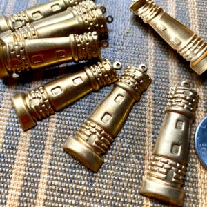 May include: A collection of eight gold-toned metal lighthouse charms. The charms are detailed with brickwork and windows.